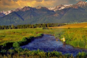 Man fly-fishing in river with mountains in the background, Oregon
